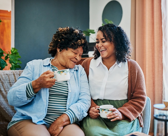 Older woman and her personal assistant laughing together over tea at home