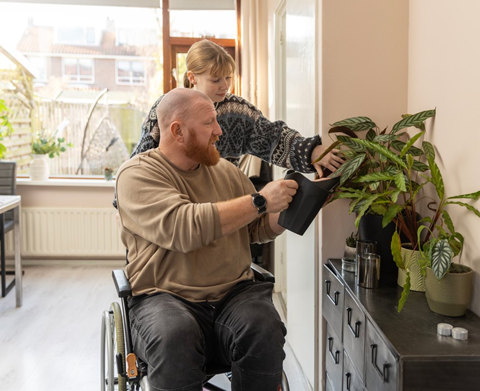 Man in a wheelchair watering houseplants at home with a child beside him
